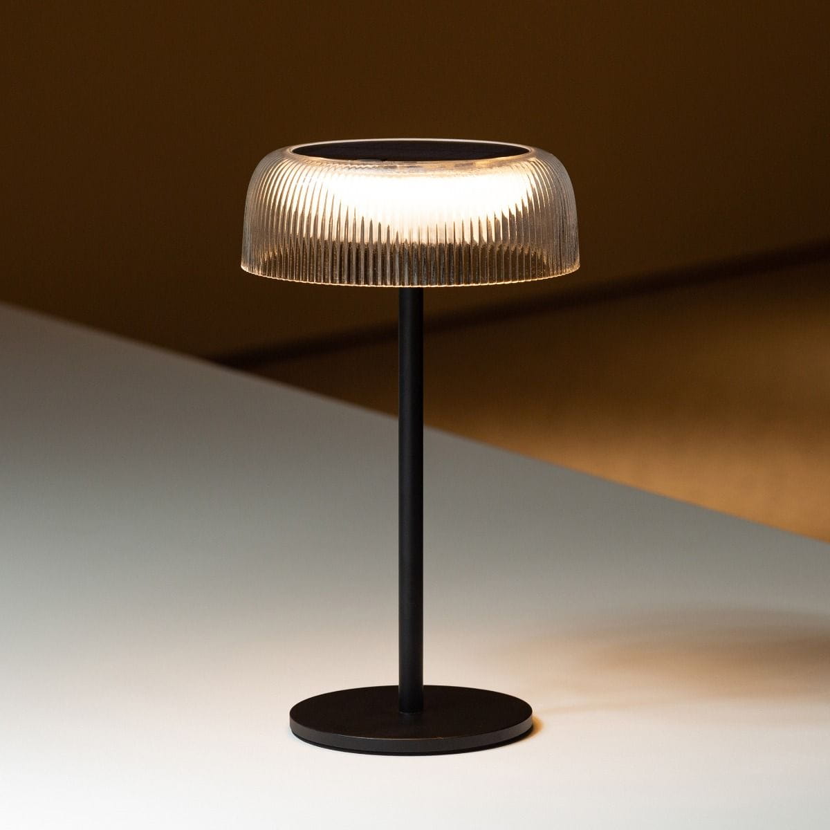Czarna lampa stołowa solarna LED Bluet o mocy 2,5W i temperaturze barwowej 3000K. Posiada szklaną, teksturowaną klosz w formie stożka, umieszczony na smukłym, metalowym stelażu z okrągłą podstawą. Idealna do użytku wewnętrznego i zewnętrznego (IP44).
