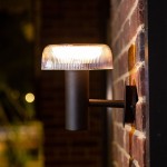 Kinkiet solarny LED 2,5W w kolorze czarnym z przezroczystym kloszem, montowany na ścianie. Okrągły kształt, z wyraźnymi żłobieniami na kloszu. Źródło światła o barwie 3000K, z klasą szczelności IP44. Ujęcie z boku, zbliżone na detal lampy.