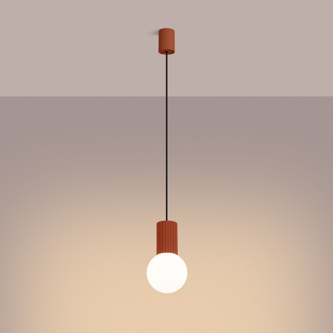 Lampa wisząca Halo z pojedynczym źródłem światła G9, w kolorze ochra czerwona. Produkt zawieszony na czarnym przewodzie, z cylindrycznym uchwytem o teksturowanej powierzchni. Kulista żarówka w dolnej części. Tło w stonowanej tonacji.
