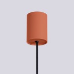 Lampa wisząca Halo o cylindrycznym kloszu w odcieniu ochry czerwonej, zawieszona na czarnym przewodzie. Klosz ma matową teksturę, a całość prezentuje się w frontalnym ujęciu na jednolitym tle.