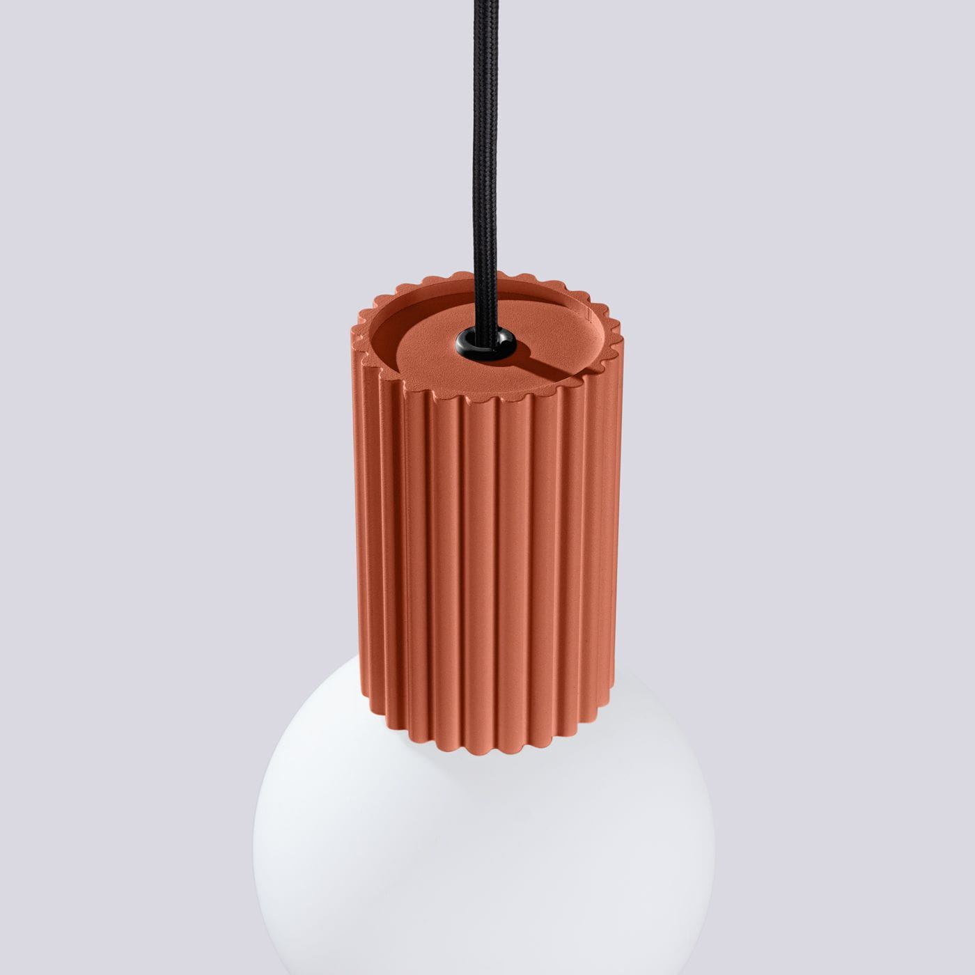 Lampa wisząca Halo z kloszem w kształcie kuli, z czerwonym, żłobionym uchwytem. Uchwyt łączy się z czarnym kablem. Tło w jasnym odcieniu szarości, podkreślające kolor i fakturę lampy. Idealna do nowoczesnych wnętrz.