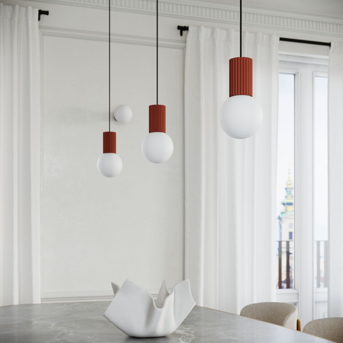 Lampa wisząca Halo z jednym źródłem światła G9, z białą kulistą kloszem i czerwonym, żeberkowanym trzonem. Zawieszona na czarnych linkach, w aranżacji z nowoczesnym stołem i ceramicznym naczyniem na tle jasnych zasłon.