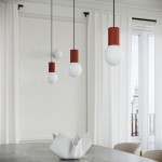 Lampa wisząca Halo z jednym źródłem światła G9, z białą kulistą kloszem i czerwonym, żeberkowanym trzonem. Zawieszona na czarnych linkach, w aranżacji z nowoczesnym stołem i ceramicznym naczyniem na tle jasnych zasłon.