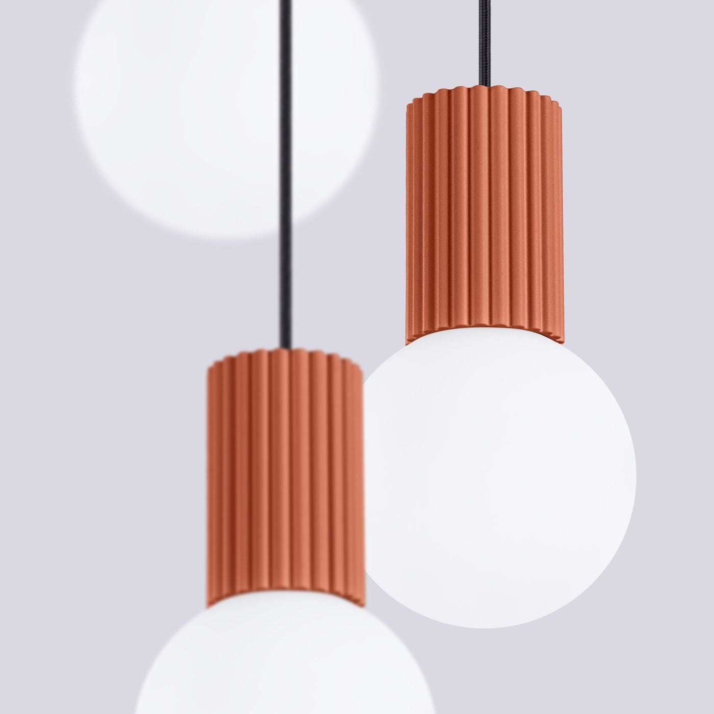 Lampa wisząca Halo z trzema źródłami światła G9, z czerwonym, żłobkowanym kloszem oraz białą, okrągłą żarówką. Produkt zawieszony na czarnym przewodzie, na jasnoszarym tle, w układzie bliskim zbliżeniu.