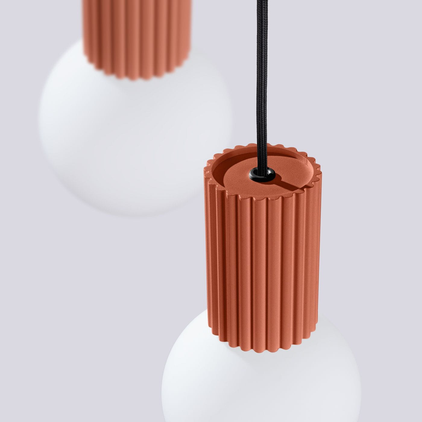 Lampa wisząca Halo 3xG9 w kolorze ochry czerwanej z matowym, białym kloszem. Wysoka, żeberkowana podstawa w kolorze ceglanym, z widocznym czarnym przewodem. Ujęcie z bliska, pokazujące detale wykończenia i kształt lampy.