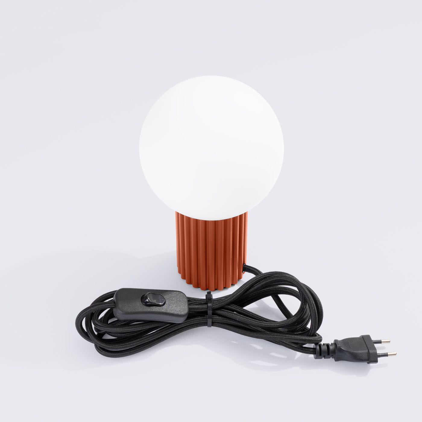 Lampa stołowa Halo 1xG9 w kolorze ochra czerwona, z okrągłym, białym kloszem i teksturowanym, cylindrycznym słupkiem. Widoczny czarny przewód z włącznikiem. Ujęcie frontalne na białym tle.