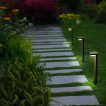 Lampa ogrodowa solarna Grid, czarna, z czujnikiem ruchu, ustawiona na ścieżce z betonowych płytek. Oświetla otoczenie, z widocznymi roślinami w tle, na trawie. Wysoka na około 50 cm, z prostokątną głowicą LED.