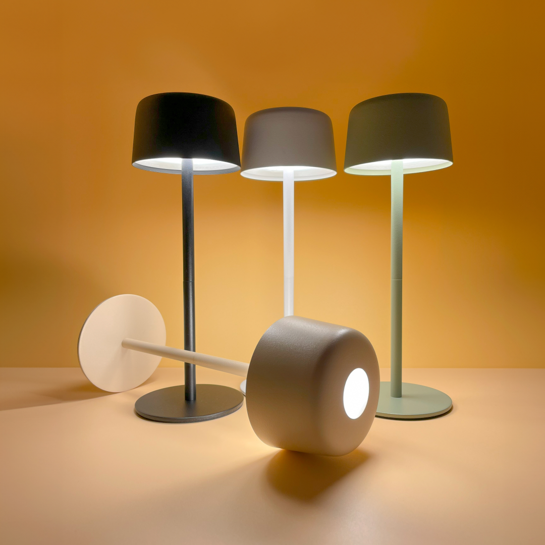 Czarna lampa stołowa LED Poco o mocy 2W i temperaturze barwowej 3000K. Posiada cylindryczny klosz i solidną podstawę. W tle widoczne inne lampy w różnych kolorach. Całość na jednolitym pomarańczowym tle.
