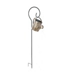 Konewka lampa solarna LED w kolorze czarnym i miedzianym, z dekoracyjnym wzorem. Ustawiona na czarnym, metalowym stelażu z haczykiem. Wbudowane źródło światła 3000K, IP44, idealna do ogrodu lub na taras.