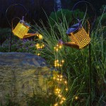 Konewka lampa solarna LED w kolorze czarnym i miedzianym, umieszczona na metalowym stelażu. Emituje ciepłe światło 3000K, ozdobiona wzorami. W tle trawa oraz kamień, a z konewki spływają drobne lampki LED. Idealna do ogrodu.