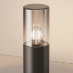 Lampa ogrodowa Amas H25 w kolorze grafitowym, z cylindrycznym korpusem i przezroczystą osłoną. Widoczna żarówka E27 z dekoracyjnym filamentem, stojąca na prostym tle.