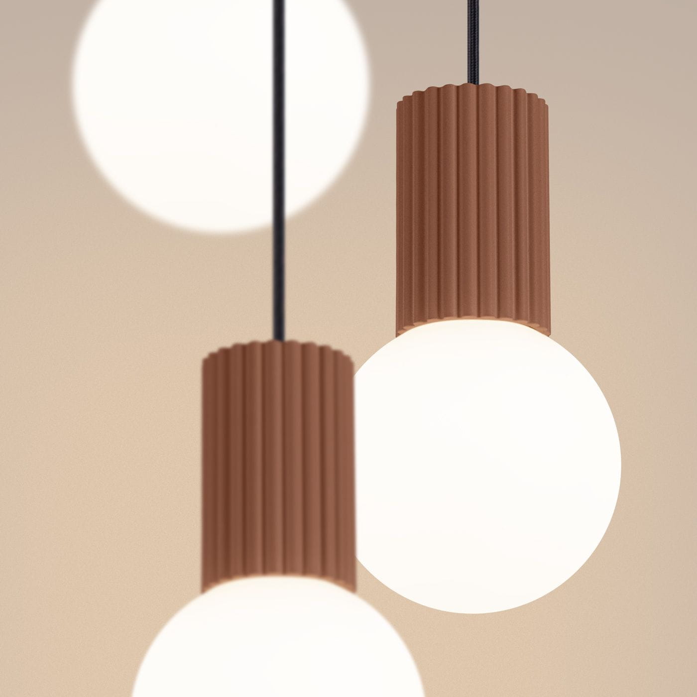 Lampa wisząca Halo z trzema źródłami światła G9. Ciemnobrązowe, żebrowane oprawy z tworzywa, z białymi, okrągłymi kloszami. Produkt wisi na czarnych przewodach, w subtelnym, jasnym tle. Idealna do nowoczesnych wnętrz.