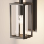 Kinkiet elewacyjny Cell w kolorze grafitowym z oprawą w kształcie prostopadłościanu. Wewnątrz widoczna żarówka E27. Produkt zamontowany na ścianie, z przezroczystymi ściankami, co umożliwia swobodne wydobywanie się światła.