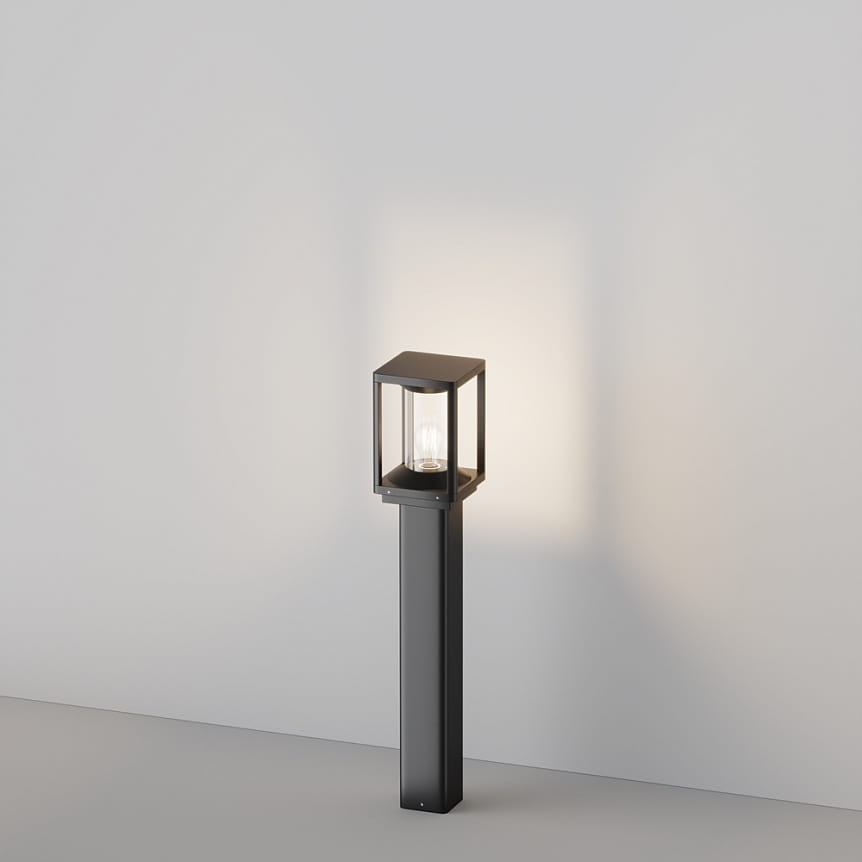 Lampa ogrodowa stojąca Cell H75 w kolorze grafitowym, z oprawą w kształcie sześcianu. Wyposażona w jedną żarówkę E27, umieszczona na prostym, kwadratowym słupku. Zdjęcie ukazuje lampę na szarym tle, oświetloną od wewnątrz.