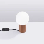 Lampa stołowa Halo z okrągłym, białym kloszem i cylindryczną podstawą w kolorze mocca. Widoczny czarny przewód z przełącznikiem. Ujęcie z boku na jasnym tle, podkreślające teksturę podstawy.