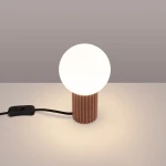 Lampa stołowa Halo z cylindrycznym, żłobkowanym podstawą w kolorze mocca oraz okrągłą, białą kloszem. Ujęcie z boku, z widocznym kablem z włącznikiem. Tło w odcieniach szaro-beżowych.