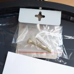 Zestaw akcesoriów montażowych do lustra podświetlanego D60, w tym metalowy wkręt i plastikowy kołek, umieszczony w przezroczystej torebce. W tle widoczny fragment lustra.