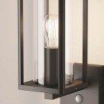 Kinkiet elewacyjny Cell w kolorze grafitowym, z czujnikiem ruchu, zawiera żarówkę E27. Obudowa wykonana z metalu z przezroczystym kloszem, montowany na ścianie. Widoczny detal czujnika ruchu na dolnej części lampy.