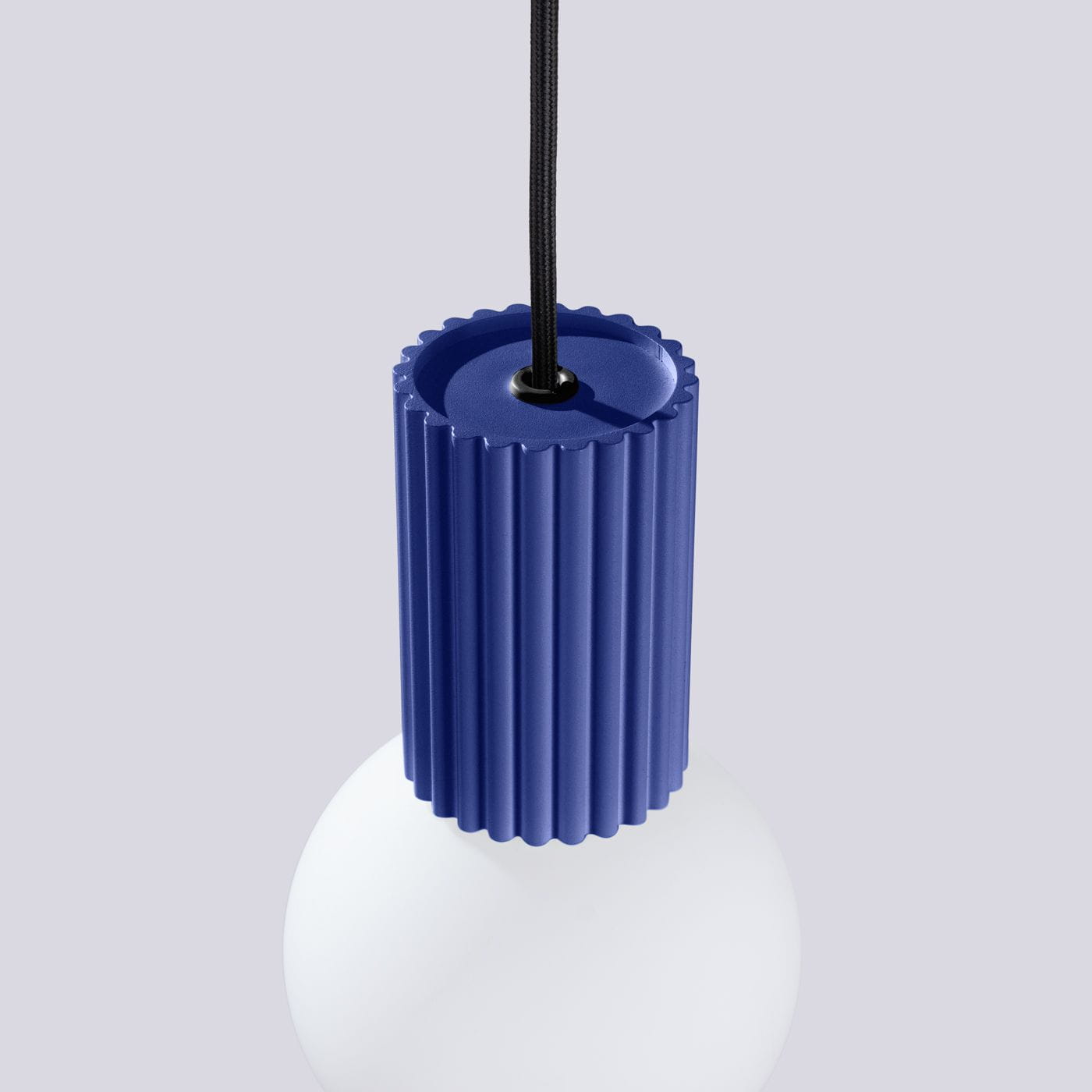 Lampa wisząca Halo w kolorze niebieskim z podłużnym, żebrowanym uchwytem oraz białą, okrągłą kloszem. Wisi na czarnym przewodzie. Widać szczegóły uchwytu i klosza w zbliżeniu, na jednolitym tle.