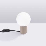 Lampa stołowa Halo w kolorze taupe z okrągłym, białym kloszem i żebrowanym, cylindrycznym podstawą. Kabel z włącznikiem w kolorze czarnym, ustawiona na płaskiej powierzchni.