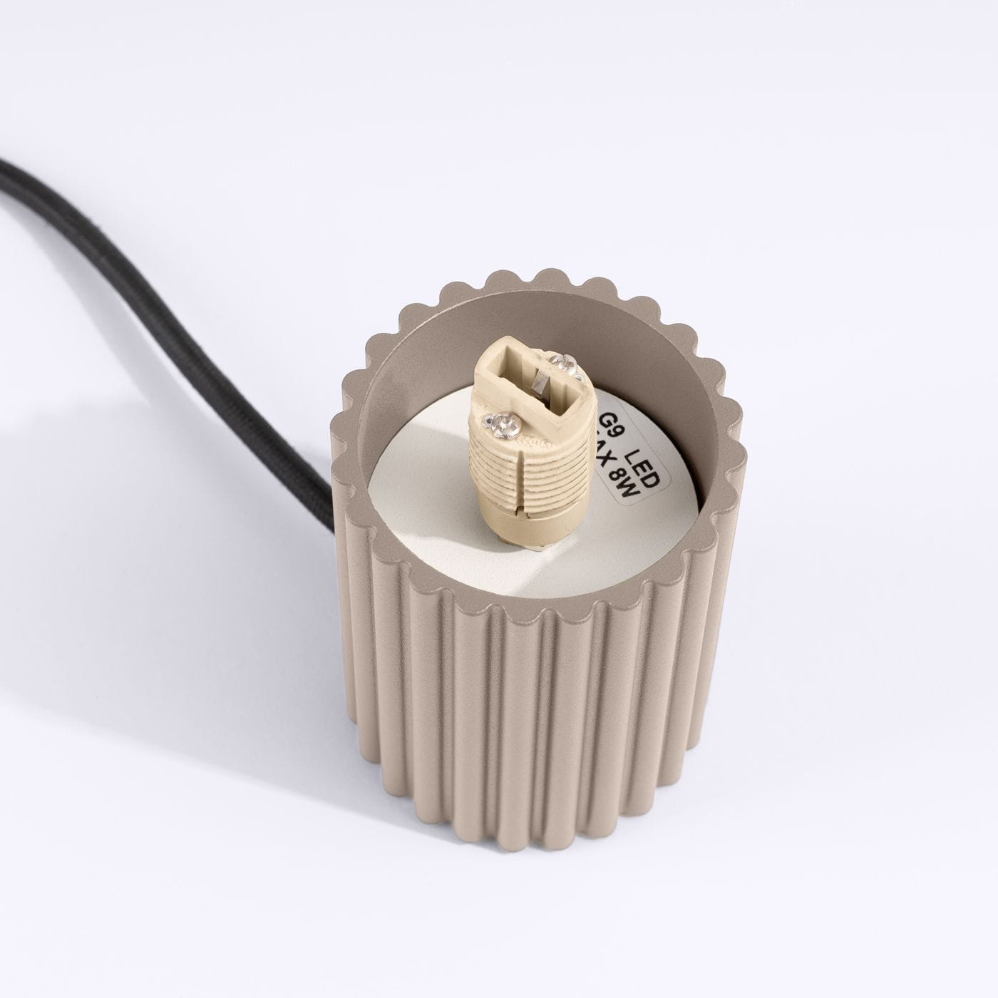 Lampa stołowa Halo w kolorze taupe, z okrągłą podstawą o falistej teksturze. Widoczny gwint G9 do żarówki LED, maks. 8W. Czarne przewody zasilające. Ujęcie z góry, ukazujące szczegóły mocowania.