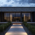 Lampa ogrodowa LED Hagen H60 5W 3000K w kolorze grafitowym, stojąca na ścieżce, emitująca ciepłe światło, otoczona zieloną roślinnością, w nowoczesnej aranżacji z widokiem na budynek.