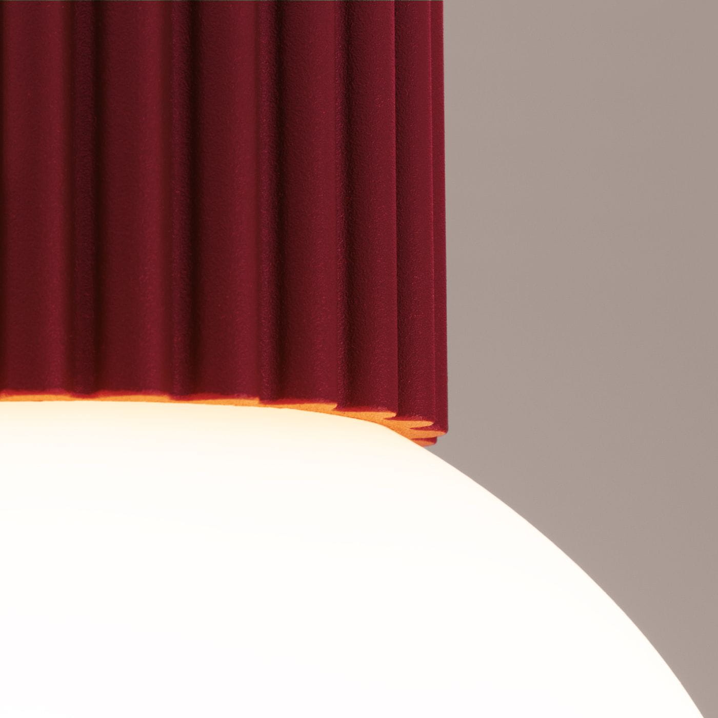 Lampa sufitowa Halo z oprawą w kolorze burgundowym, z fakturowanym, żebrowanym wykończeniem u góry oraz zaokrąglonym, białym kloszem. Widać dolną część lampy, która emituje światło.