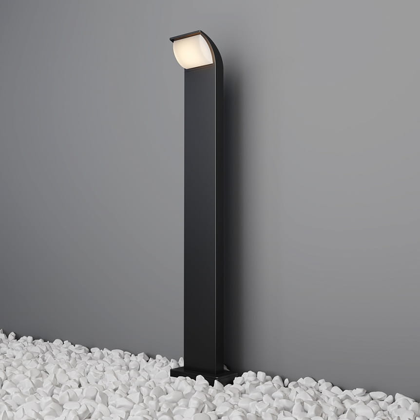 Lampa ogrodowa LED Stock H80 w kolorze grafitowym, o wysokości 80 cm, z ujęciem frontalnym. Wyposażona w źródło światła 7W, emituje ciepłe światło 3000K. Prosta, smukła konstrukcja z lekko zaokrąglonym kloszem, umieszczona na białych kamieniach.