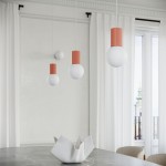 Lampa wisząca Halo w kolorze brzoskwiniowym z białymi kloszami, zawieszona w grupie trzech elementów na cienkich linkach. Widoczny matowy klosz oraz dekoracyjny, prążkowany uchwyt. Lampa znajduje się nad stołem, w jasnym wnętrzu z oknami i zasłonami.