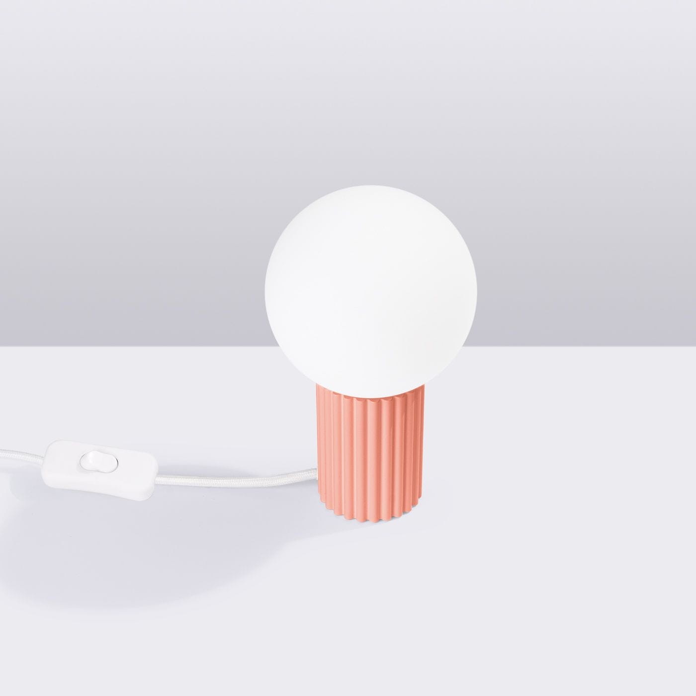 Lampa stołowa Halo 1xG9 z brzoskwiniowym, teksturowanym korpusem i okrągłą, białą kloszem. Widoczne przewody z przyciskiem włącz/wyłącz. Ujęcie z boku, na jasnym tle.