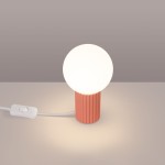 Brzoskwiniowa lampa stołowa Halo z podstawą w prążki i okrągłą, białą kloszem. Ujęcie z boku, z widocznym kablem z przełącznikiem. Lampa stoi na jasnej powierzchni, na jednolitym tle.