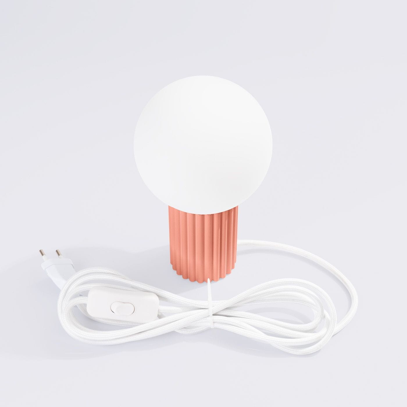 Lampa stołowa Halo 1xG9 w kolorze brzoskwiniowym z okrągłą, białą głowicą. Podstawa z delikatnym, teksturowanym wykończeniem. Widoczny biały kabel z włącznikiem. Ujęcie frontalne na białym tle.