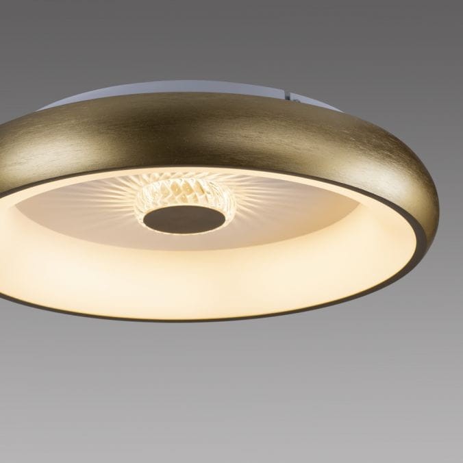 Plafon LED Vertigo o mocy 29W w kolorze mosiądzu, z okrągłą, płaską podstawą oraz wbudowanym źródłem światła. Widoczny detal wzoru w kloszu, umożliwiający rozpraszanie światła. Produkt z pilotem do zdalnego sterowania.