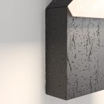 Kinkiet elewacyjny LED 12W 3000K w kolorze czarnym, o prostokątnym kształcie. Materiał z teksturą, z widocznymi kroplami wody. Zainstalowany na ścianie, emitujący ciepłe światło.