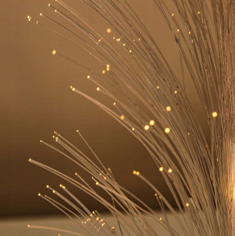 Lampa solarna ogrodowa w kształcie trawy, wbijana, z wysokością 80 cm. Wyposażona w cienkie włókna emitujące ciepłe światło LED, o delikatnej, przezroczystej fakturze. Ujęcie z bliska pokazujące detale świecących końcówek włókien.