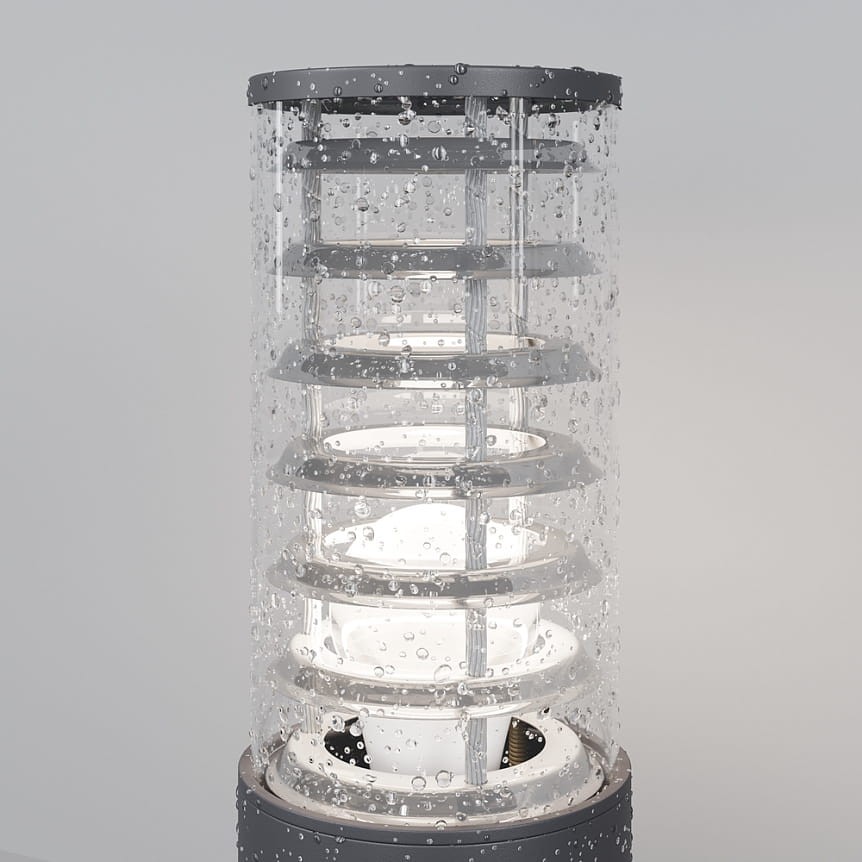 Grafitowa lampa ogrodowa Bronx H80 z oprawą 1xE27, z przezroczystym kloszem z efektem kropli wody, w pionowej pozycji, z widocznymi elementami wewnętrznymi i metalową podstawą. Idealna do oświetlenia przestrzeni zewnętrznych.