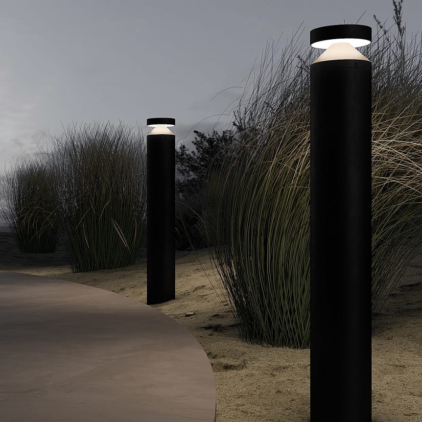 Lampa ogrodowa LED Olten H80 w kolorze grafitowym, wysokość 80 cm. Wbudowana lampa o mocy 12W, temperatura barwowa 3000K. Ustawiona pionowo na ścieżce, w otoczeniu trawy, na tle zmierzchu. Górna część z przezroczystym kloszem.