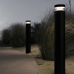 Lampa ogrodowa LED Olten H80 w kolorze grafitowym, wysokość 80 cm. Wbudowana lampa o mocy 12W, temperatura barwowa 3000K. Ustawiona pionowo na ścieżce, w otoczeniu trawy, na tle zmierzchu. Górna część z przezroczystym kloszem.
