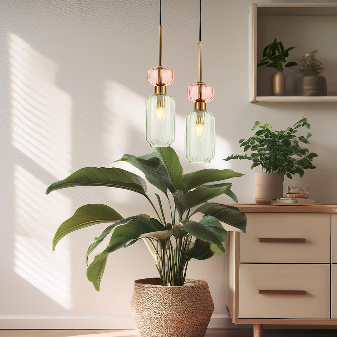Lampa wisząca Molly 1xE14 w kolorze złotym i zielonym, z przezroczystym kloszem i różowym detalem. Zawieszona na cienkim kabelku, w tle rośliny doniczkowe i minimalistyczne meble.
