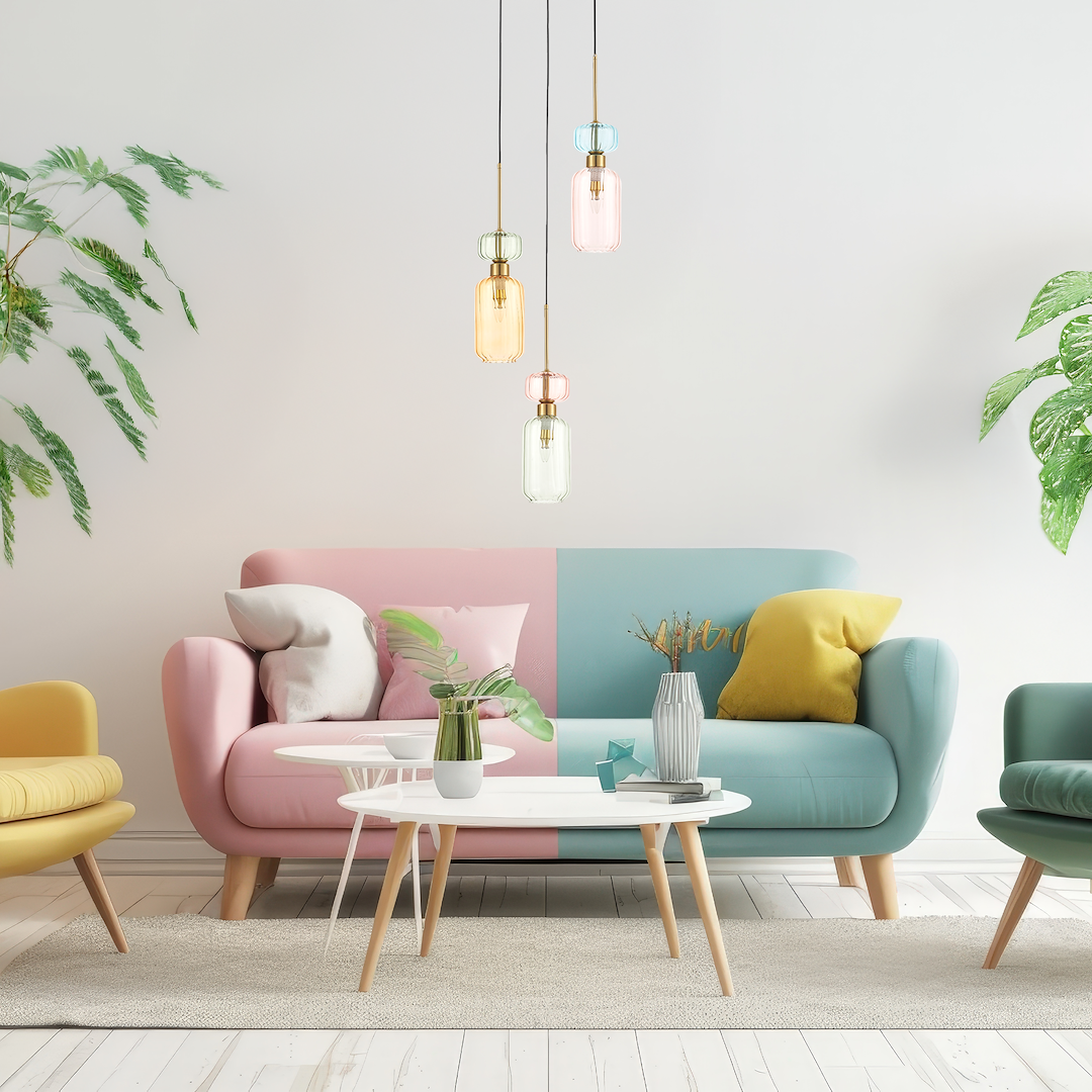 Lampa wisząca Molly 3xE14 w kolorze złotym z mixem szklanych kloszy w odcieniach pomarańczowym, różowym i zielonym. Zawieszona nad jasnym, nowoczesnym stolikiem w aranżacji z kolorowym sofą i roślinami w tle.