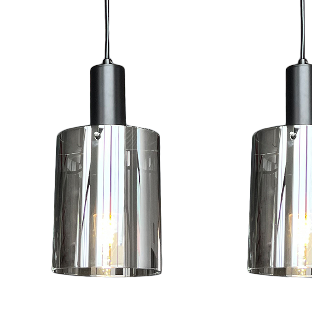 Czarna lampa wisząca Arcadia Black z trzema oprawami E27. Szklane klosze o cylindrycznym kształcie, z transparentnym wykończeniem, zawieszone na czarnym przewodzie. Lampa ma nowoczesny design, idealna do wnętrz.