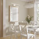 Kinkiet Prado L60 LED 11W 3000K w kolorze białym, zamontowany na ścianie nad białą ramą lustra. Oświetlenie w minimalistycznym stylu, idealne do aranżacji wnętrz. Widoczne elementy drewnianego stołu i krzeseł w jasnym kolorze.
