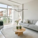 Lampa wisząca LED Ambar 35W 4000K w kolorze czarnym, o minimalistycznym kształcie, zawieszona nad okrągłym stołem. Tło to nowoczesny salon z jasnymi ścianami, szarym sofą i roślinnymi dekoracjami w wazonie.