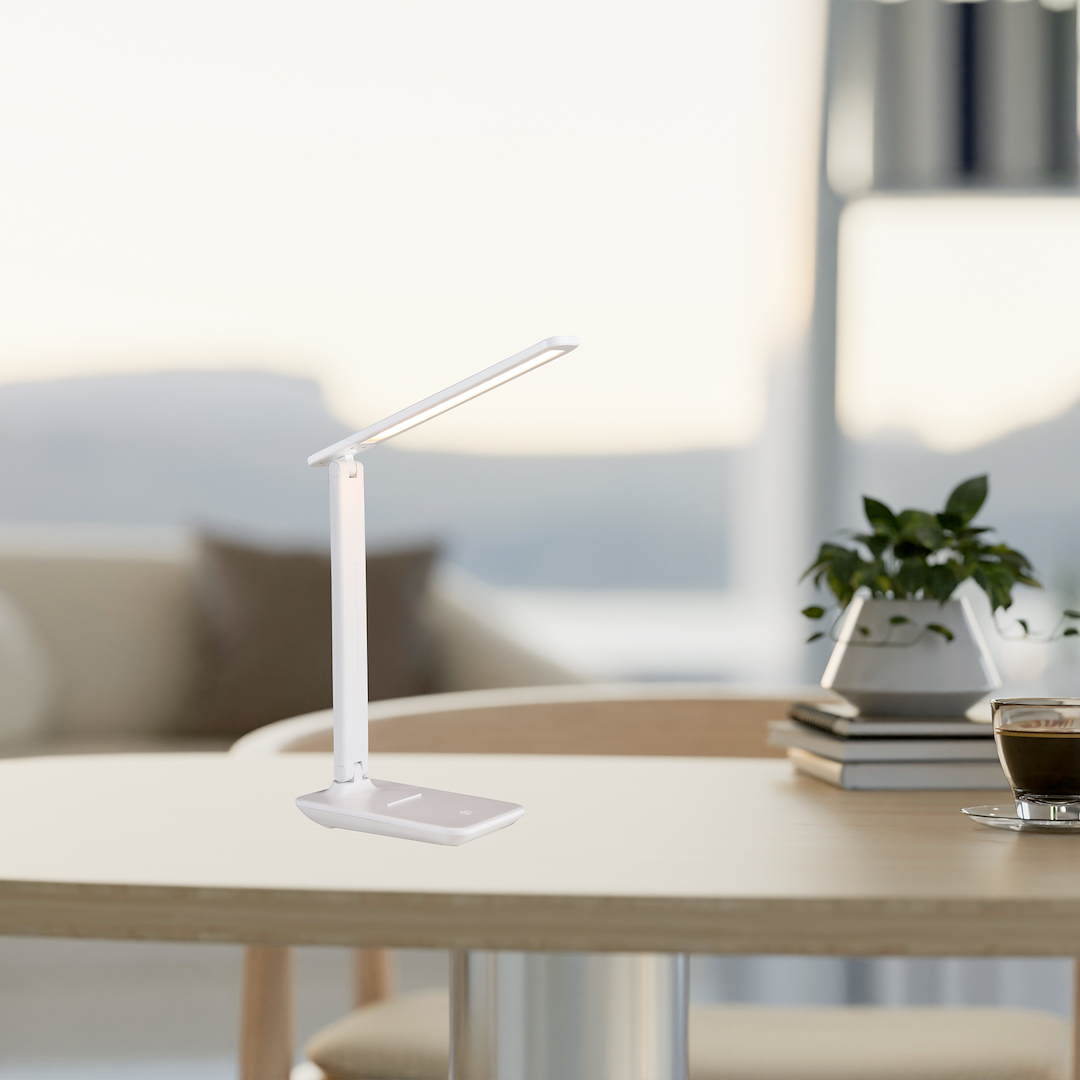 Lampa biurkowa LED 5W CCT w kolorze białym. Produkt stoi na okrągłym blacie, z prostą, smukłą konstrukcją i regulowanym ramieniem. W tle widać kwiaty oraz filiżankę kawy, co tworzy domową atmosferę.