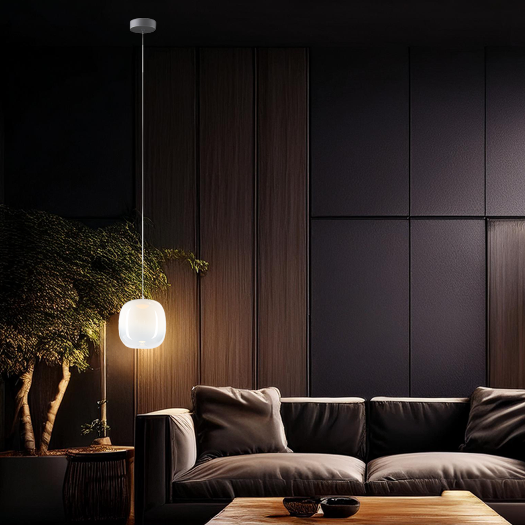 Lampa wisząca LED Vaso 2 l, 4W, 3000K, biała, zawieszona na cienkim przewodzie w nowoczesnym wnętrzu. Oświetlenie emituje ciepłe światło, a tło stanowi ciemna ściana oraz wygodna, ciemna kanapa. W pobliżu roślina doniczkowa.