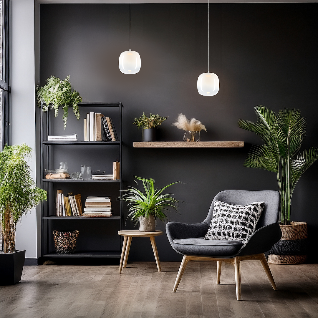 Lampa wisząca LED Vaso 2 l o mocy 4W i barwie 3000K, w białym, szklanym kloszu, zawieszona w nowoczesnym wnętrzu z ciemną ścianą. W tle półka z roślinami, książkami oraz wygodny fotel z poduszką.