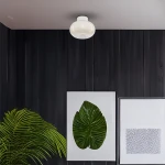 Lampa sufitowa LED Vaso o mocy 4W, kolor biała, w kształcie zaokrąglonej kulki, zamontowana na suficie. W tle ciemne drewniane ściany, z boku zielona roślina i dwa obrazy na białych ramach. Jasne światło o temperaturze 3000K.
