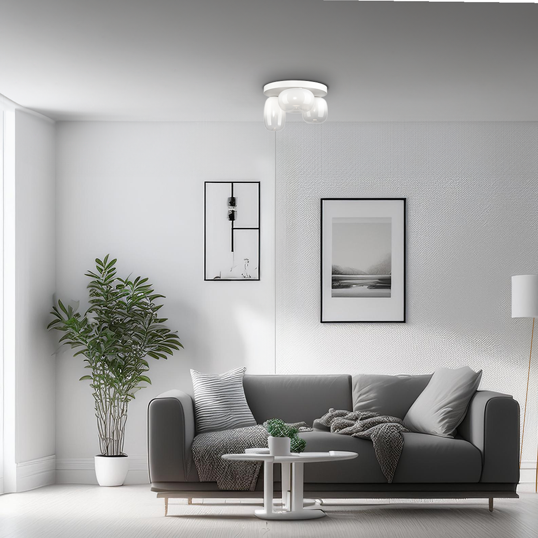 Lampa sufitowa LED Vaso 12W 3000K w białej obudowie, z trzema zaokrąglonymi kloszami. Zawieszona na suficie w jasnym wnętrzu, w otoczeniu kanapy i rośliny. Umożliwia równomierne oświetlenie przestrzeni.
