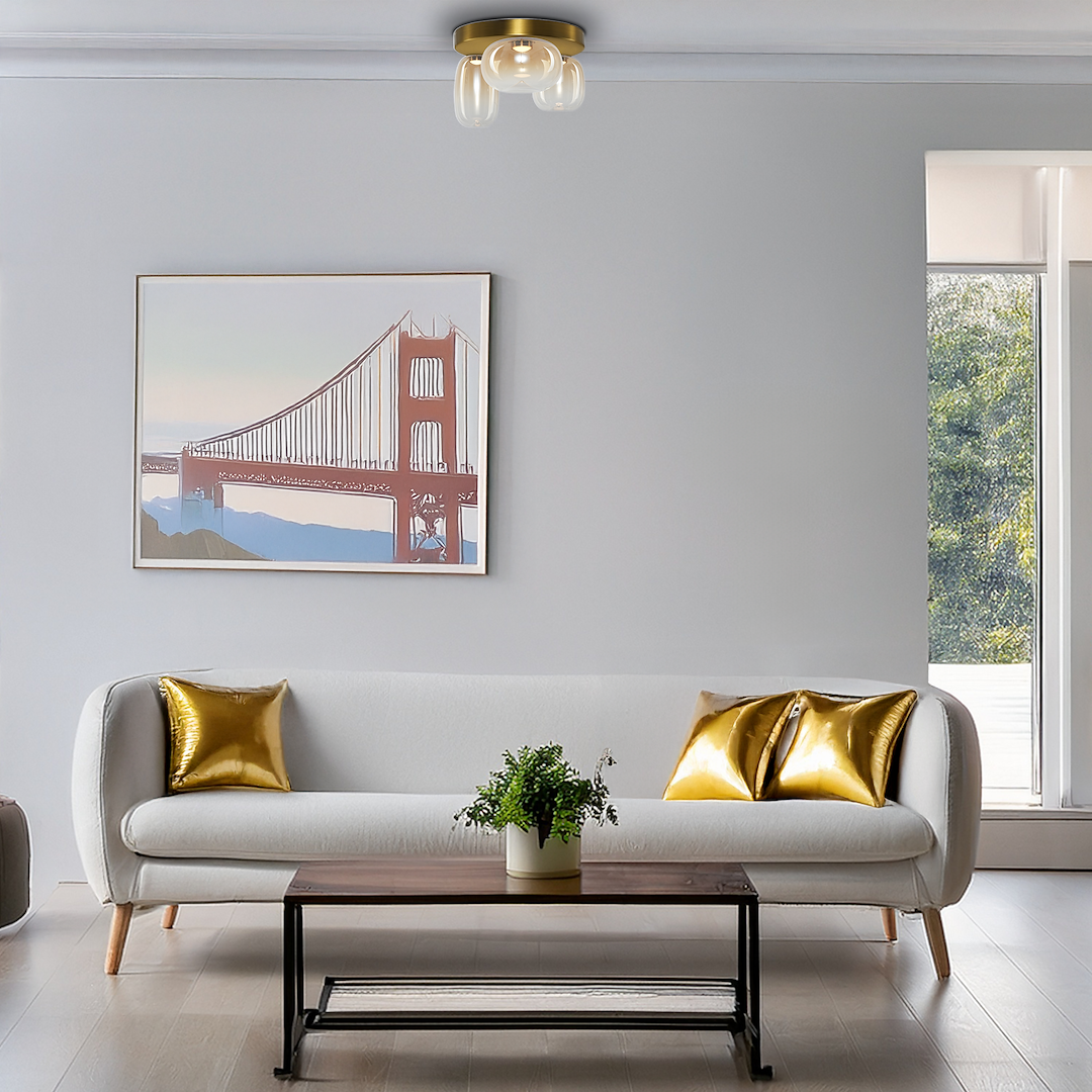 Lampa sufitowa LED Vaso 12W 3000K w kolorze złotym i bursztynowym, z okrągłym, metalowym kloszem. Zawieszona na suficie, w nowoczesnym wnętrzu z białą sofą i złotymi poduszkami. Obraz w tle przedstawia most Golden Gate.
