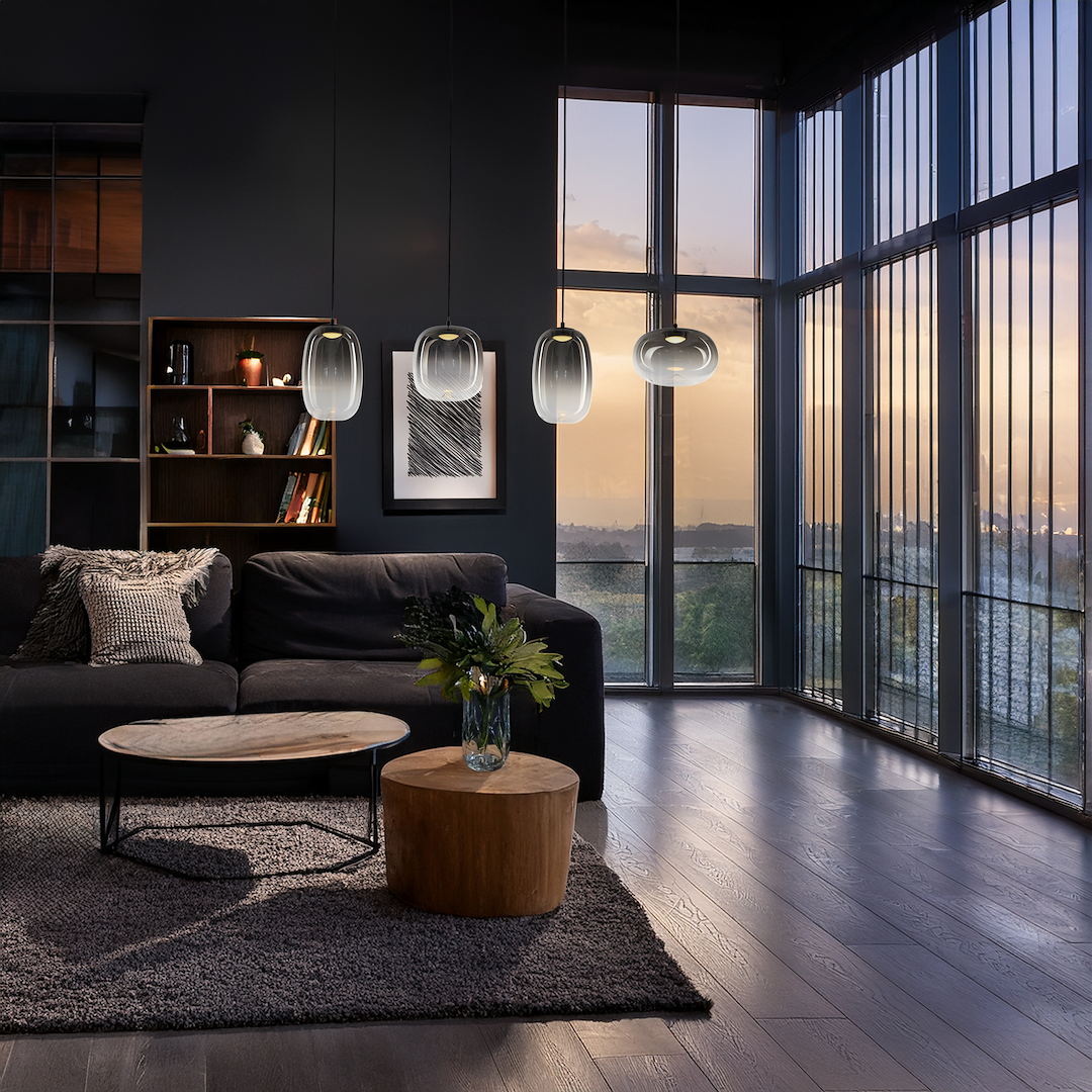 Lampa wisząca LED Vaso 15W 3000K w kolorze czarnym i dymionym, zawieszona w nowoczesnym wnętrzu. Widoczne są cztery lampy nad sofą, w otoczeniu drewnianych mebli i dużych okien. Ciepłe światło tworzy przytulną atmosferę.
